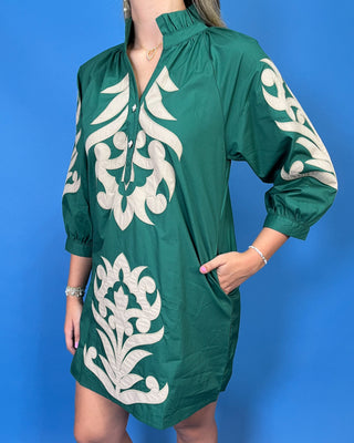 A woman wearing a green short-sleeve tunic dress with large white embroidered floral motifs