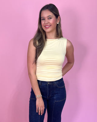 Woman wearing a light yellow sleeveless top and dark blue jeans against a pink background