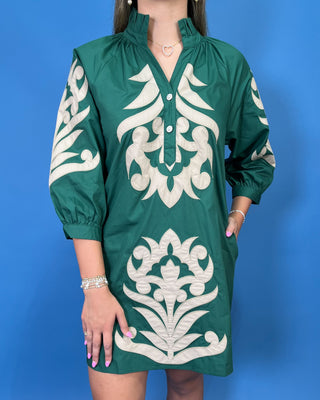 A woman wearing a green short-sleeve tunic dress with large white embroidered patterns