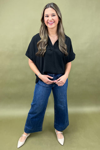 Woman wearing a black top and blue jeans against a green background
