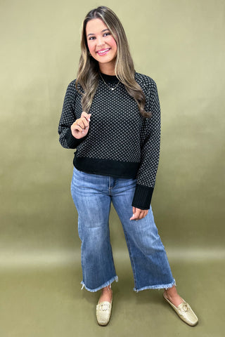 Woman wearing a black patterned sweater and blue jeans against a green background