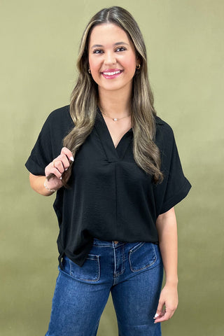 Woman wearing a black top and blue jeans against a green background