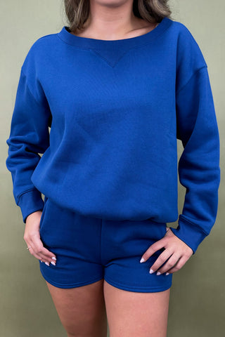 Person wearing a blue sweatshirt and shorts set against a green background