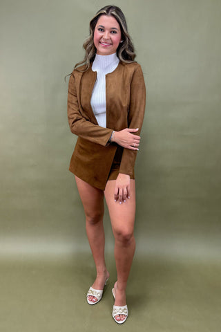 Woman wearing a brown jacket and skirt set against a green background