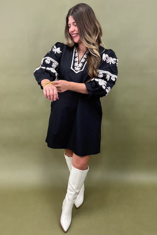 Woman wearing a black dress with white floral patterns and white knee-high boots on a green background