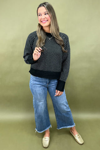 Woman wearing a black patterned sweater and blue jeans against a green background
