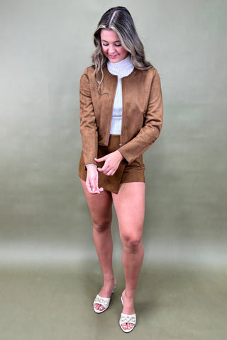 Woman wearing a brown jacket and skirt set against a green background