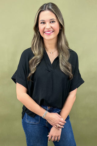 Woman wearing a black top and blue jeans against a green background