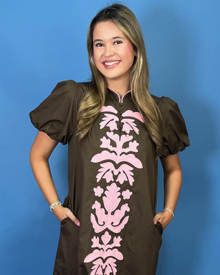 A woman modeling a brown midi dress with puff sleeves and a pink damask pattern down the front
