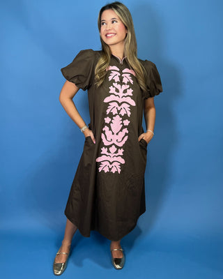 A woman modeling a brown midi dress with puff sleeves and a pink damask pattern down the front