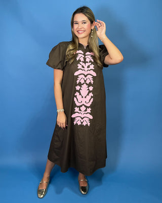 A woman modeling a brown midi dress with puff sleeves and a pink damask pattern down the front