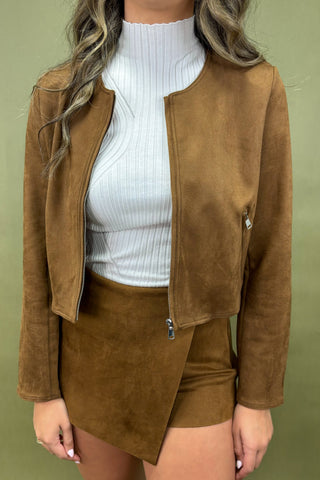 Person wearing a brown suede jacket and shorts set with a white top on a green background