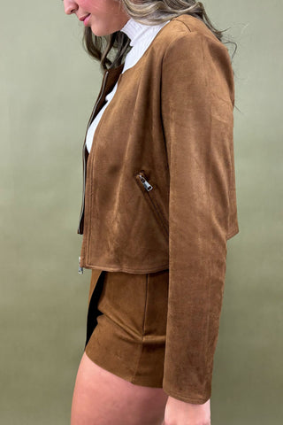 Woman wearing a brown jacket and skirt set against a green background