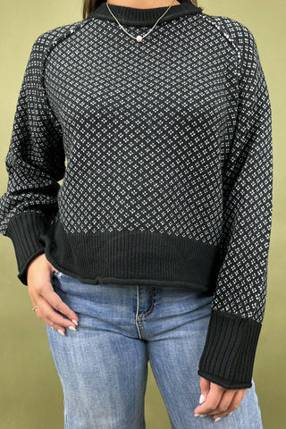 Person wearing a black and white patterned sweater with blue jeans against a green background