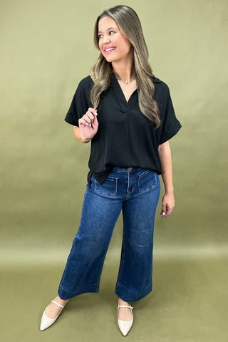 Woman wearing a black top and blue jeans against a green background