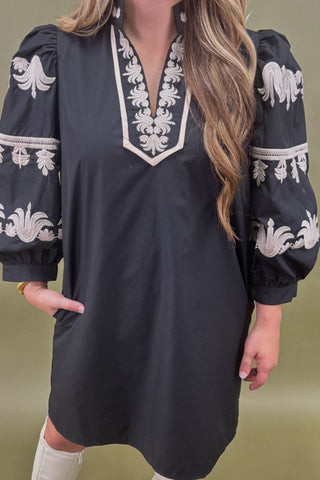 Black dress with white embroidery worn by a person on a green background
