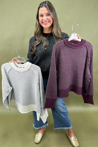 Woman holding two sweaters on hangers against a green background
