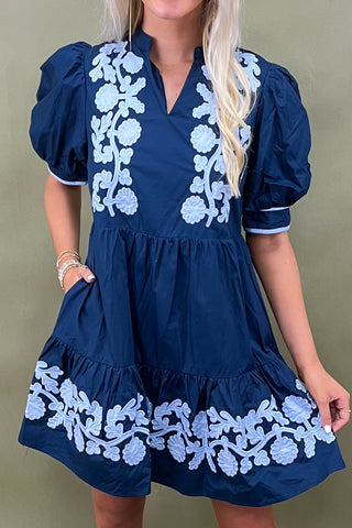Navy blue dress with white floral embroidery on a plain background