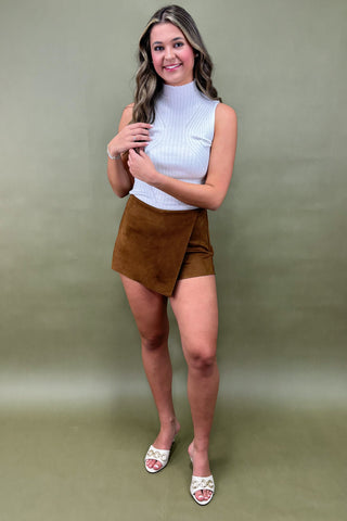 Woman wearing a white turtleneck and brown skirt against a green background