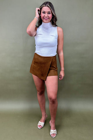 Woman wearing a white turtleneck and brown skirt against a plain background