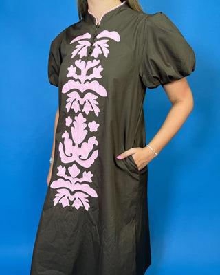 A woman wearing a dark brown or black short-sleeve dress with a vertical pink floral pattern down the front
