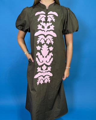 A woman wearing a dark olive green dress with a vertical pink damask pattern down the front,