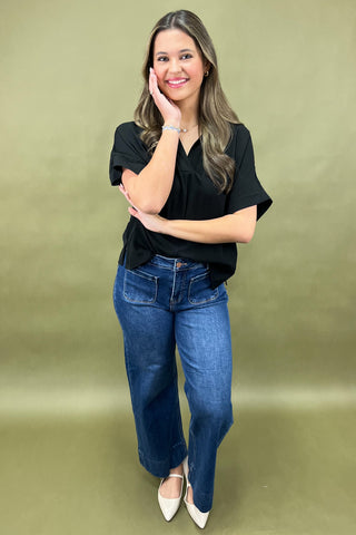 Woman wearing a black top and blue jeans against a green background