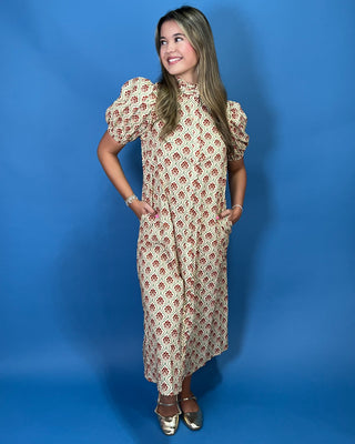 A woman modeling a cream-colored midi dress with a red and green geometric pattern, puffed short sleeves, and a high neckline