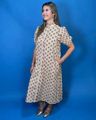 A woman modeling a short-sleeve midi dress with a beige base and a repeating red and green floral pattern