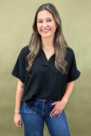 Woman wearing a black top and blue jeans against a green background