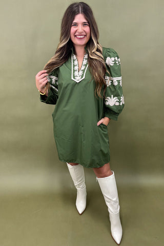 Woman wearing a green dress with white patterns and white boots against a green background