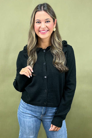 Woman wearing a black top and blue jeans against a green background
