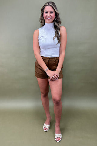 Woman wearing a white sleeveless top and brown shorts against a plain background