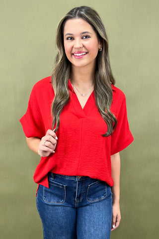 Woman wearing a red blouse and blue jeans against a green background