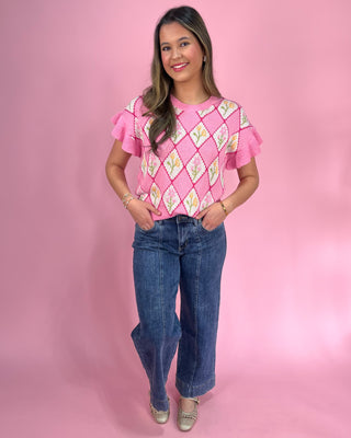 Woman wearing a pink patterned top and blue jeans against a pink background