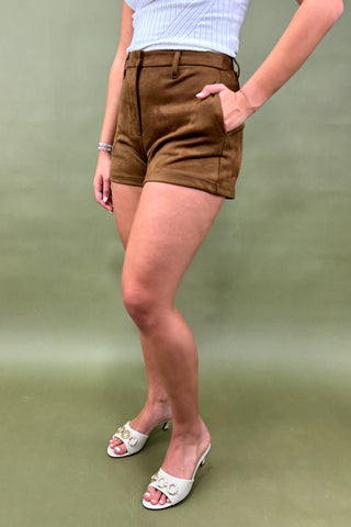 Woman wearing a white sleeveless top and brown shorts against a plain background