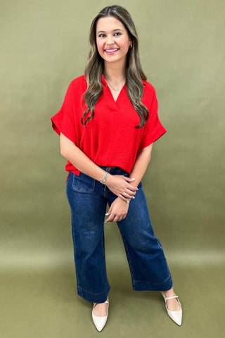 Woman wearing a red blouse and blue jeans against a green background