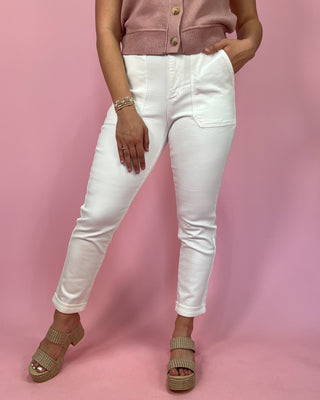 Person wearing a pink cardigan, white pants, and sandals on a pink background