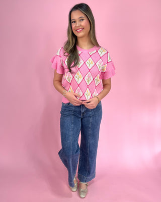 Woman wearing a pink patterned top and blue jeans on a pink background