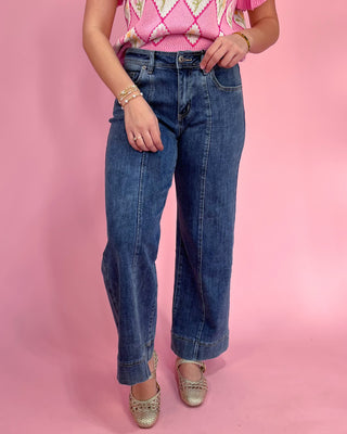 Person wearing blue jeans and a pink patterned top on a pink background