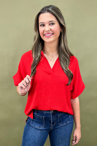 Woman wearing a red blouse and blue jeans against a green background