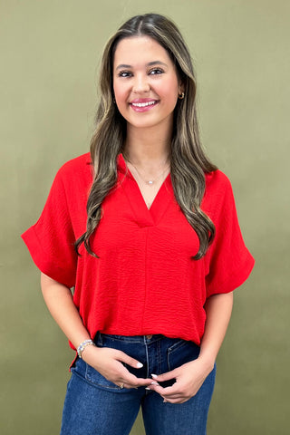 Woman wearing a red blouse and blue jeans against a green background