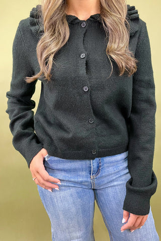 Person wearing a dark green button-up cardigan and blue jeans on a yellow background