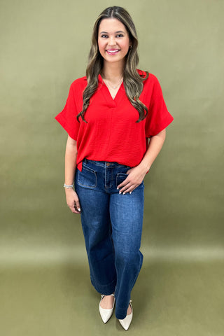 Woman wearing a red blouse and blue jeans against a green background