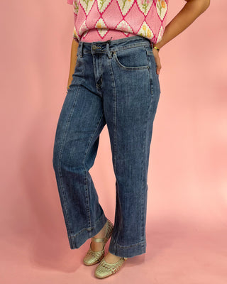Person wearing blue jeans and a pink patterned top on a pink background