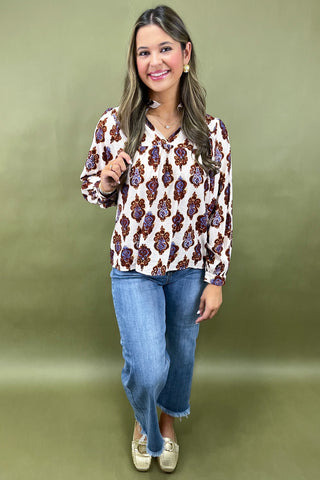 Woman wearing a patterned blouse and jeans against a green background