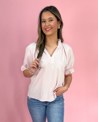 Woman wearing a white blouse with ruffled sleeves against a pink background