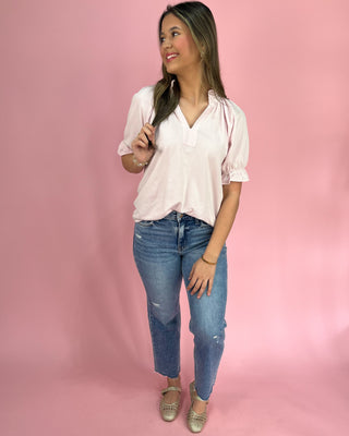 Woman wearing a light pink blouse and blue jeans against a pink background