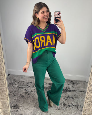 Woman taking a mirror selfie wearing a colorful sports jersey and green pants.