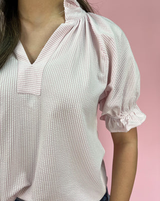 Close-up of a person wearing a light pink textured blouse against a pink background